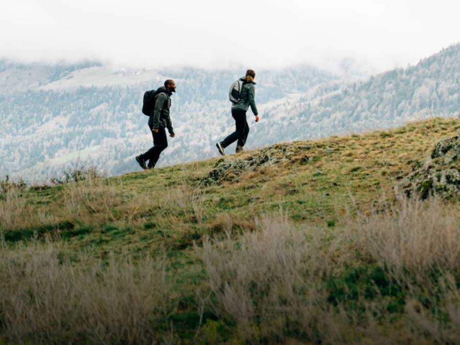 Dos personas con ropa de senderismo otoñal caminan por una montaña.
