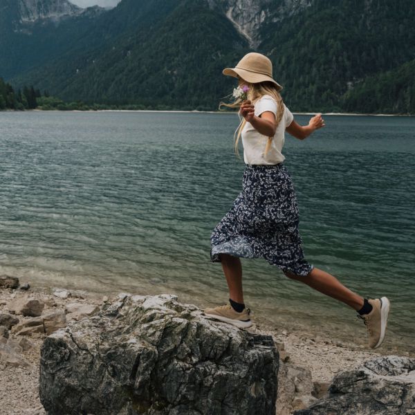 Una mujer en prendas veraniegas para actividades al aire libre balancea sobre una piedra a orillas de un lago