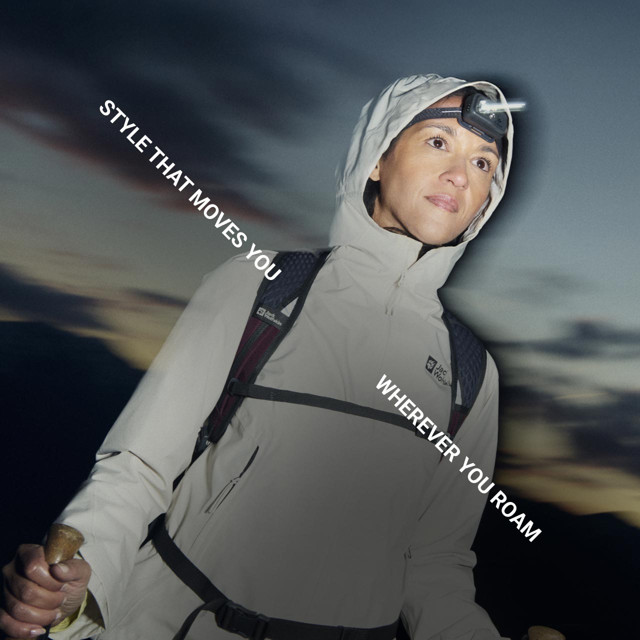Una persona en equipamiento outdoor y con una linterna frontal mira hacia delante y muestra sus bastones de senderismo mientras se pone el sol sobre las montañas. El texto dice: «Style that moves you wherever you roam»