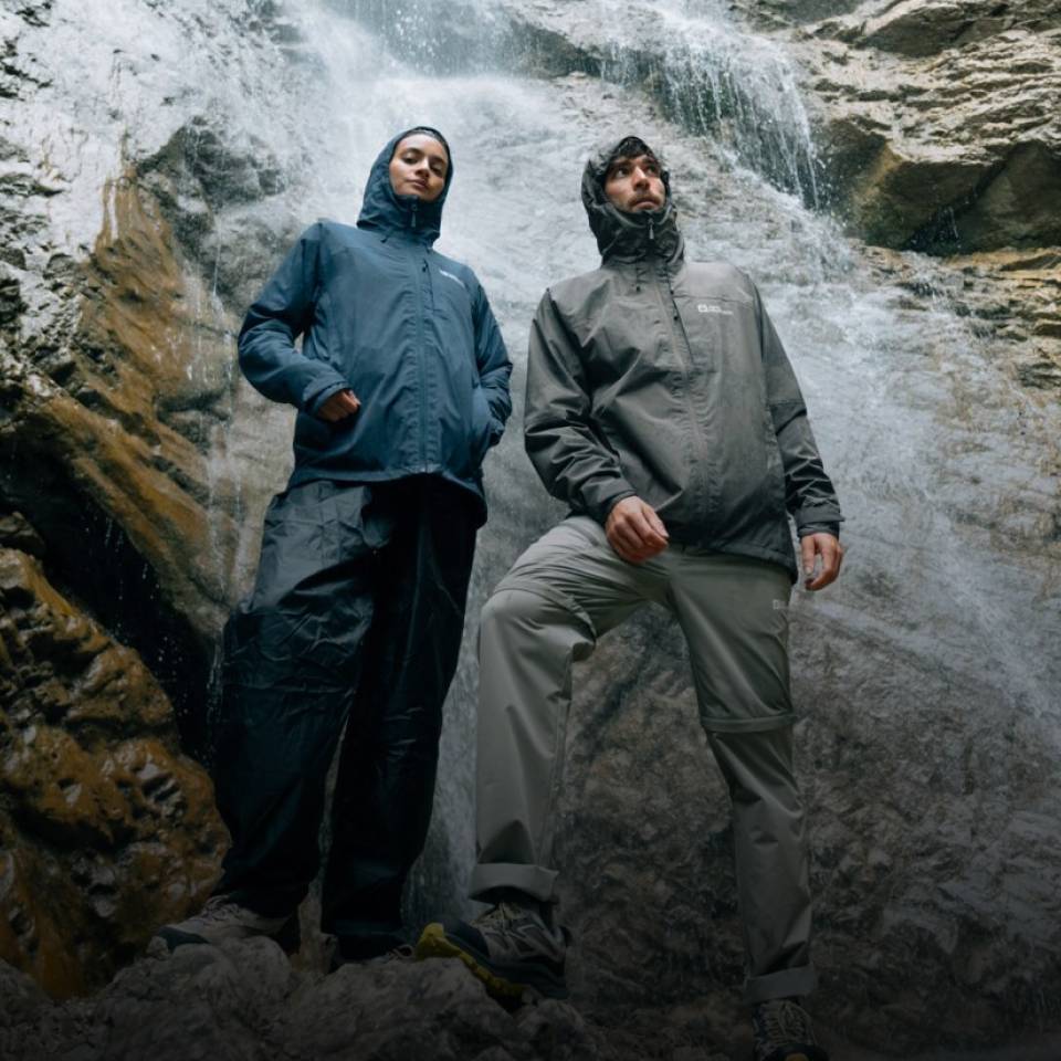Dos excursionistas con chubasqueros deportivos frente a una cascada