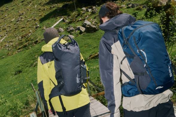 Dos senderistas con mochilas vistos por atrás que cruzan un puente de madera