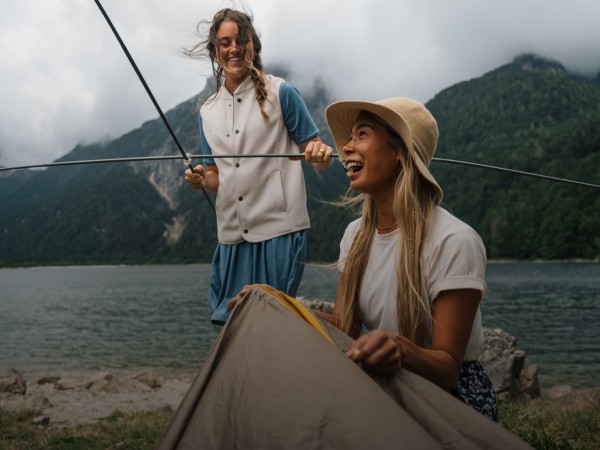 Dos mujeres sonrientes montan una tienda de campaña en un paisaje alpino