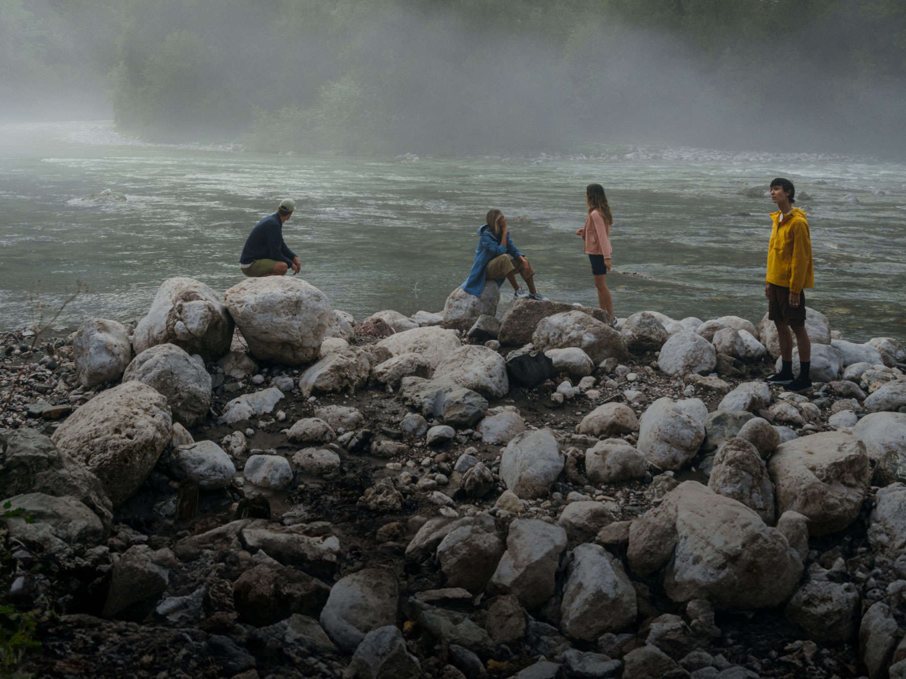 Un paisaje con niebla a orillas de un río y cuatro personas sobre unas piedras