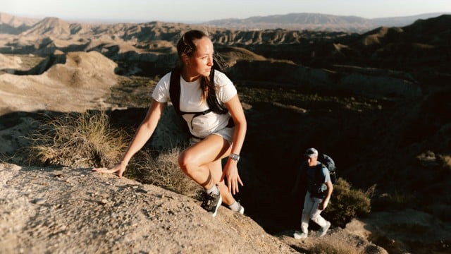 Una mujer y un hombre, con prendas de senderismo veraniegas, trepando por una roca